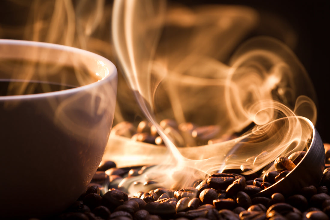 Pile of coffee beans next to a steaming cup of brewed coffee