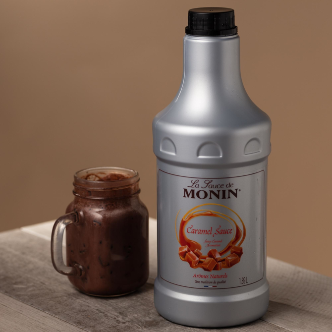 Bottle of Monin Caramel Sauce next to a jar of caramel sauce on a beige background