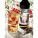 Glass of raspberry tea with ice and raspberries, Monin raspberry tea syrup bottle, and dried tea leaves on a white surface.