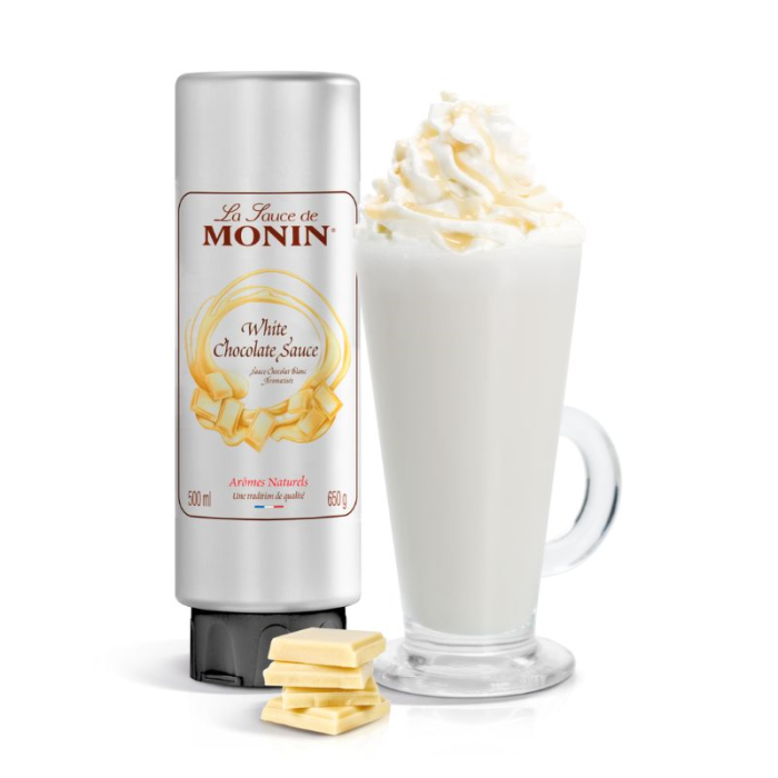 Monin white chocolate sauce bottle with a glass of white chocolate drink and white chocolate pieces on a white background