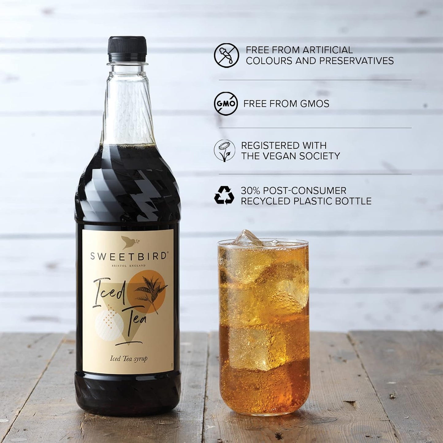 Bottle of Sweetbird Iced Tea with a glass of iced tea on a wooden surface, featuring sustainability certifications.