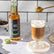 Barista-style coffee being poured into a glass mug with a bottle of Tate & Lyle syrup in the background.