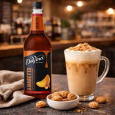 DaVinci Gourmet Amaretto syrup bottle with a glass of coffee and cookies on a bar counter.